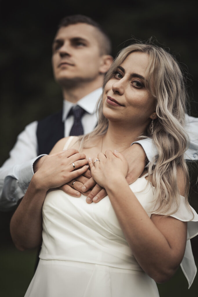 Fotograf ślubny Sosnowiec – pan młody obejmujący pannę młodą od tyłu, skupienie na splecionych dłoniach z obrączkami.