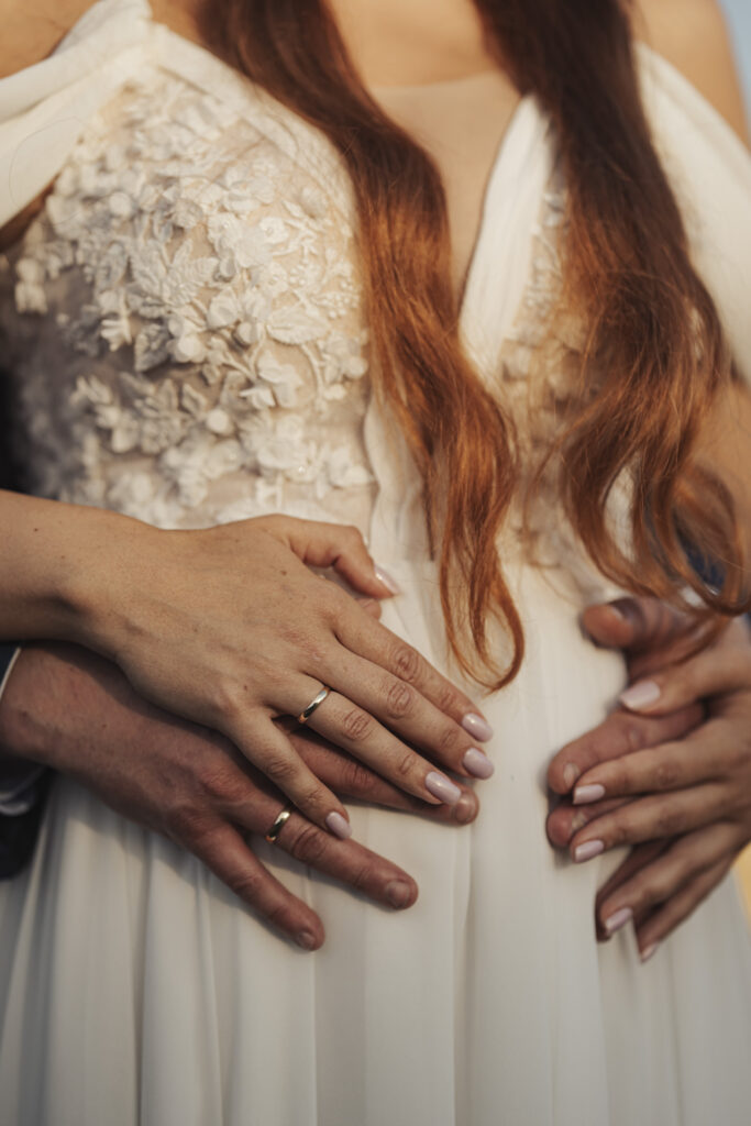 Fotografia ślubna Dąbrowa Górnicza – zbliżenie na dłonie nowożeńców na tle koronkowej sukni ślubnej, symbol bliskości.