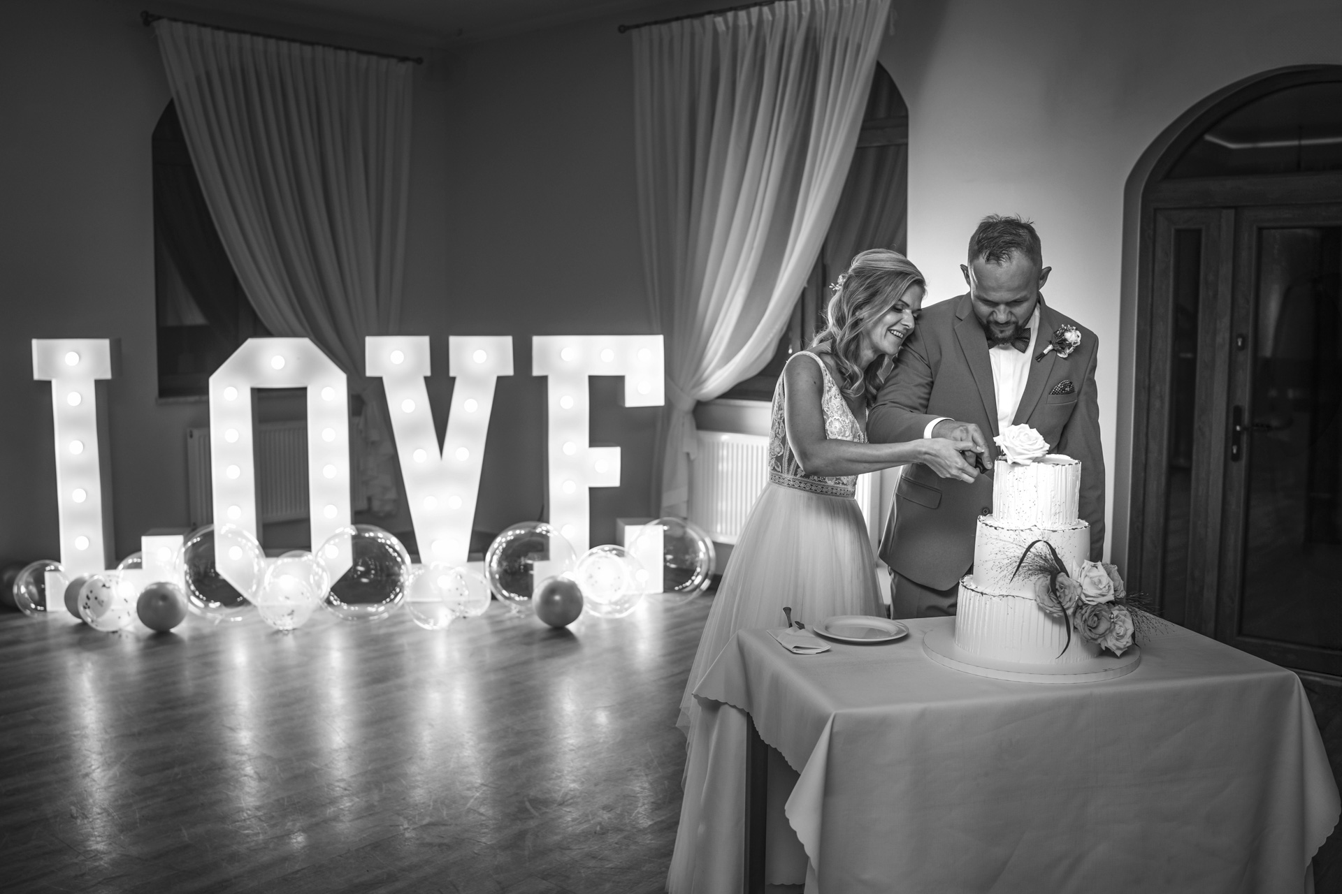 Fotografia ślubna Ruda Śląska – para młoda krojąca tort weselny przy napisie LOVE w klimacie black & white.