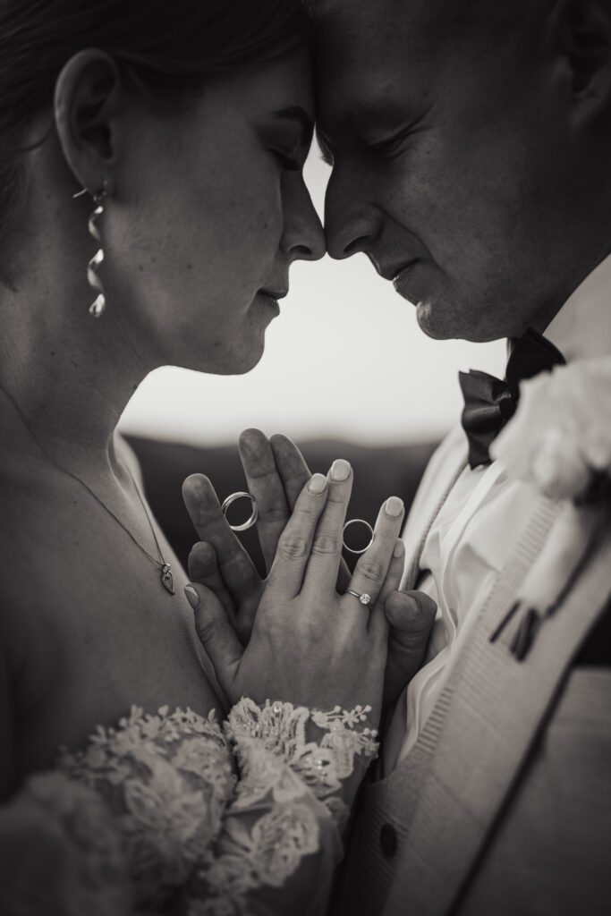 Fotograf ślubny Świętochłowice – czarno-białe, bliskie ujęcie dłoni pary młodej trzymającej obrączki przy złączonych czołach.