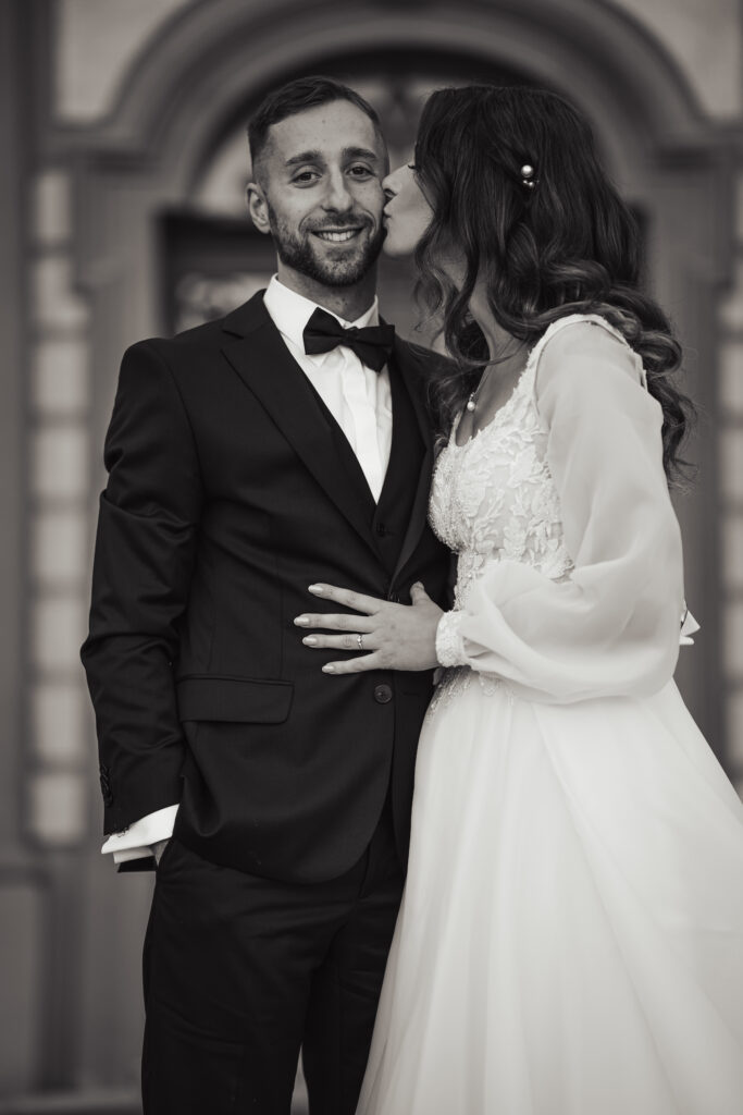 Fotografia ślubna Tychy – czarno-biały portret panny młodej całującej pana młodego w policzek.