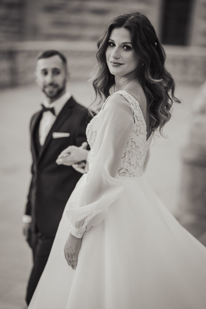 Fotografia ślubna Świętochłowice – czarno-białe zdjęcie panny młodej prowadzonej za rękę, spoglądającej z uśmiechem przez ramię.